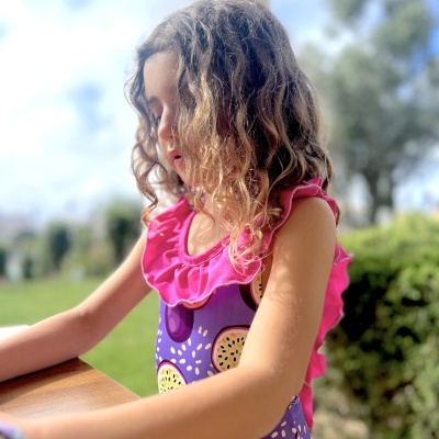 Menina de fato de banho roxo com estampa de bagas e folhos cor-de-rosa ao ar livre