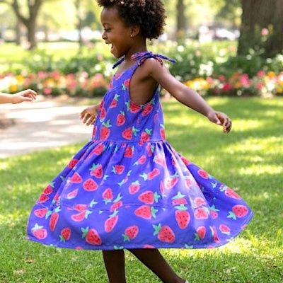 Vestido azul com padrão de morangos em criança a girar num parque