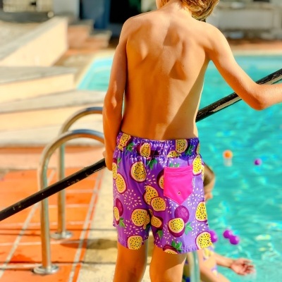 Calções de banho roxos com estampa de maracujás e bolso rosa, criança junto a piscina