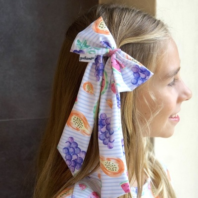 Laço de tecido colorido com padrão de frutas preso ao cabelo de uma menina.
