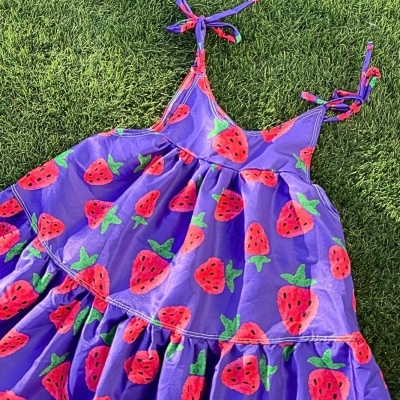 Vestido roxo infantil com estampa de morangos sobre relva verde.