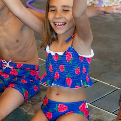 Menina com fato de banho azul com padrão de morangos vermelhos à beira de piscina