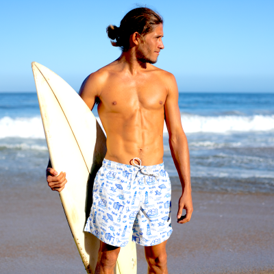 Homem com calções de banho brancos com padrão azul e prancha de surf na praia