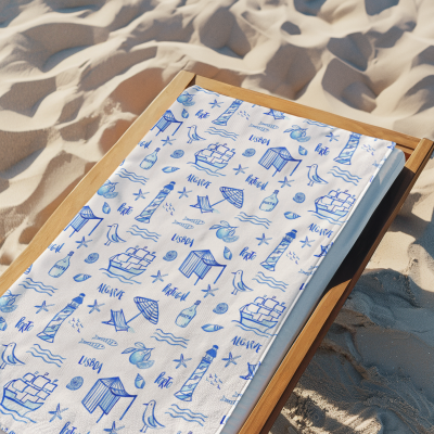 Toalha branca com desenhos azuis de símbolos portugueses numa espreguiçadeira de madeira sobre areia de praia