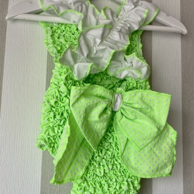 Body de bebé verde limão com folhos e laço grande, pendurado em cabides brancos