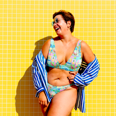 Mulher com fato de banho colorido e camisa às riscas em frente a parede amarela