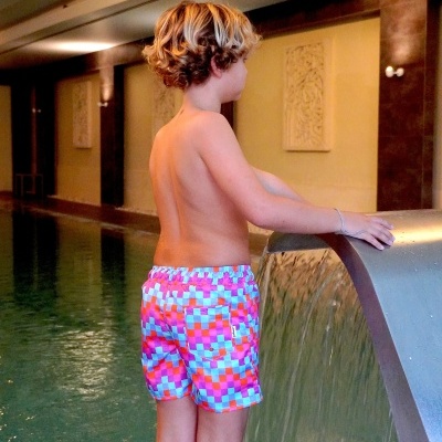 Rapaz com calções de banho coloridos junto a jato de água numa piscina interior