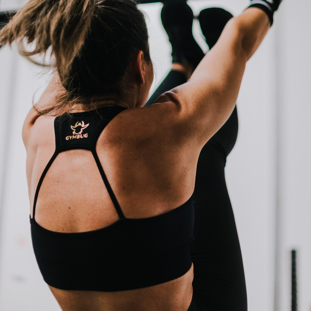 Mulher de costas a usar top desportivo preto com etiqueta GYMBUG, em ambiente de ginásio