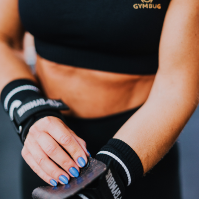 Pessoa com luvas desportivas pretas e top preto com logótipo GYMBUG amarelo