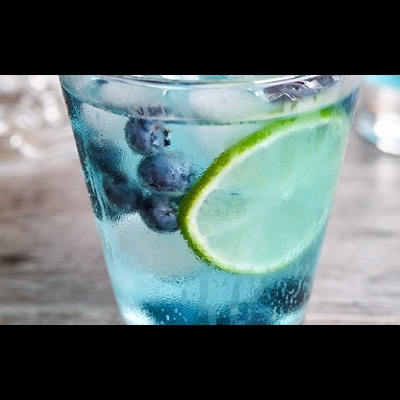 Copo de vidro com bebida azul, gelo, mirtilos e rodela de lima