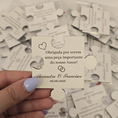 Peça de puzzle branca com texto impresso em português, segurada por mão com unha lilás, com várias peças semelhantes ao fundo