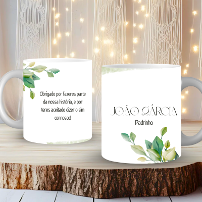 Duas canecas brancas decoradas com folhas verdes e texto personalizado, sobre uma superfície de madeira clara e fundo iluminado com luzes.