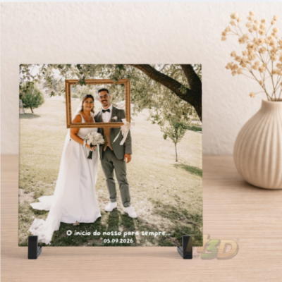 Placa acrílica com foto de noivos e texto de data do casamento em suporte preto sobre mesa com vaso e flores secas