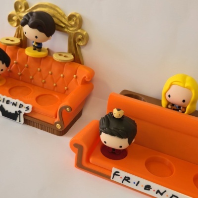 Figuras colecionáveis em sofás laranja com texto FRIENDS