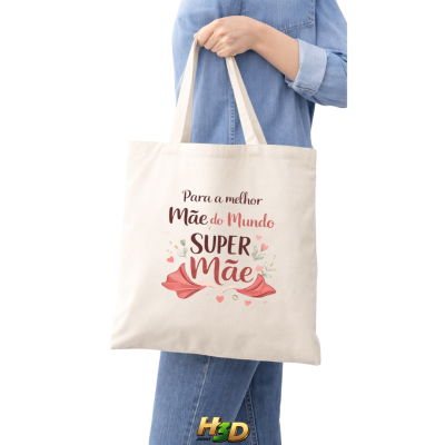 Mala de tecido bege com texto colorido para mãe, sendo segurada por pessoa com roupa jeans.