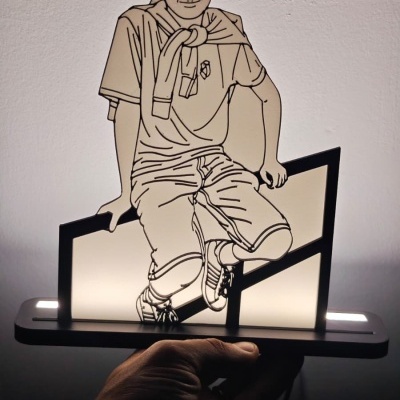 Luminária decorativa com figura de rapaz sentado em vidro ou acrílico iluminado.