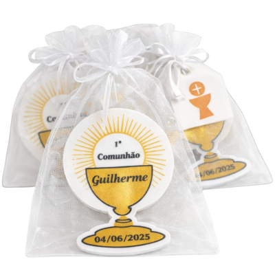 Lembranças de 1ª Comunhão embaladas em saquinhos de organza brancos com cálice dourado e texto personalizado.