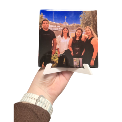 Moldura quadrada com suporte branco contendo fotografia de quatro pessoas ao ar livre