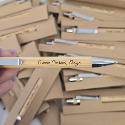 Caneta de madeira com gravação personalizada e clip metálico prateado sobre caixas de cartão castanhas