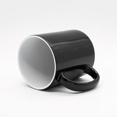 Caneca preta brilhante com interior branco deitada sobre fundo branco