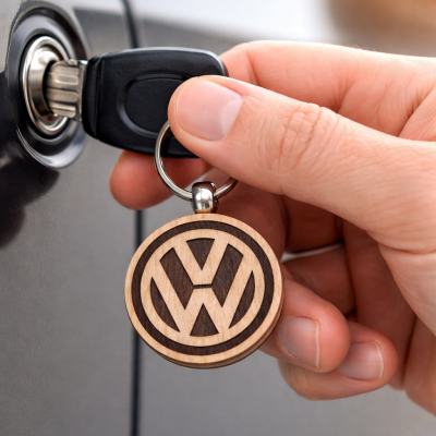 Chave de carro com chaveiro de madeira VW sendo inserida na fechadura de um carro cinza