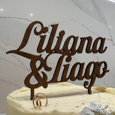 Bolo branco com topper de nomes Liliana & Tiago em material castanho e flores brancas decorativas
