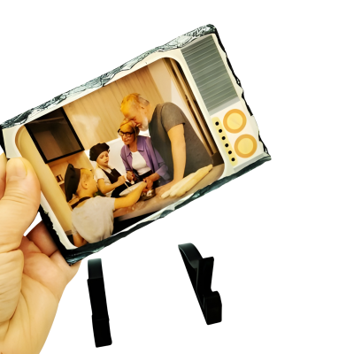 Fotografia impressa de família a cozinhar, segurada por mão, duas bases pretas no fundo.