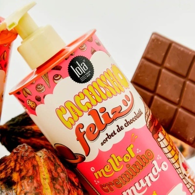 Frasco de loção corporal Lola Cosmetics com tema de chocolate, barra de chocolate e vagem de cacau ao fundo
