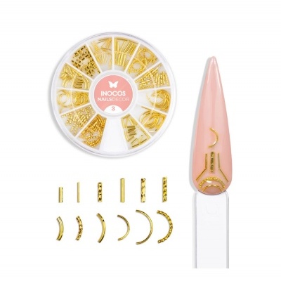 Conjunto de decoração para unhas dourada INCOS NAILSDESIGN com várias peças pequenas e uma unha amostra cor rosa nude.