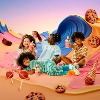 Quatro crianças com roupa colorida segurando bebidas lácteas sentadas em cenário de gelado com cookies e pirulitos.