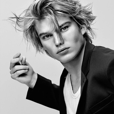 Jovem loiro com casaco preto e t-shirt branca em fundo claro