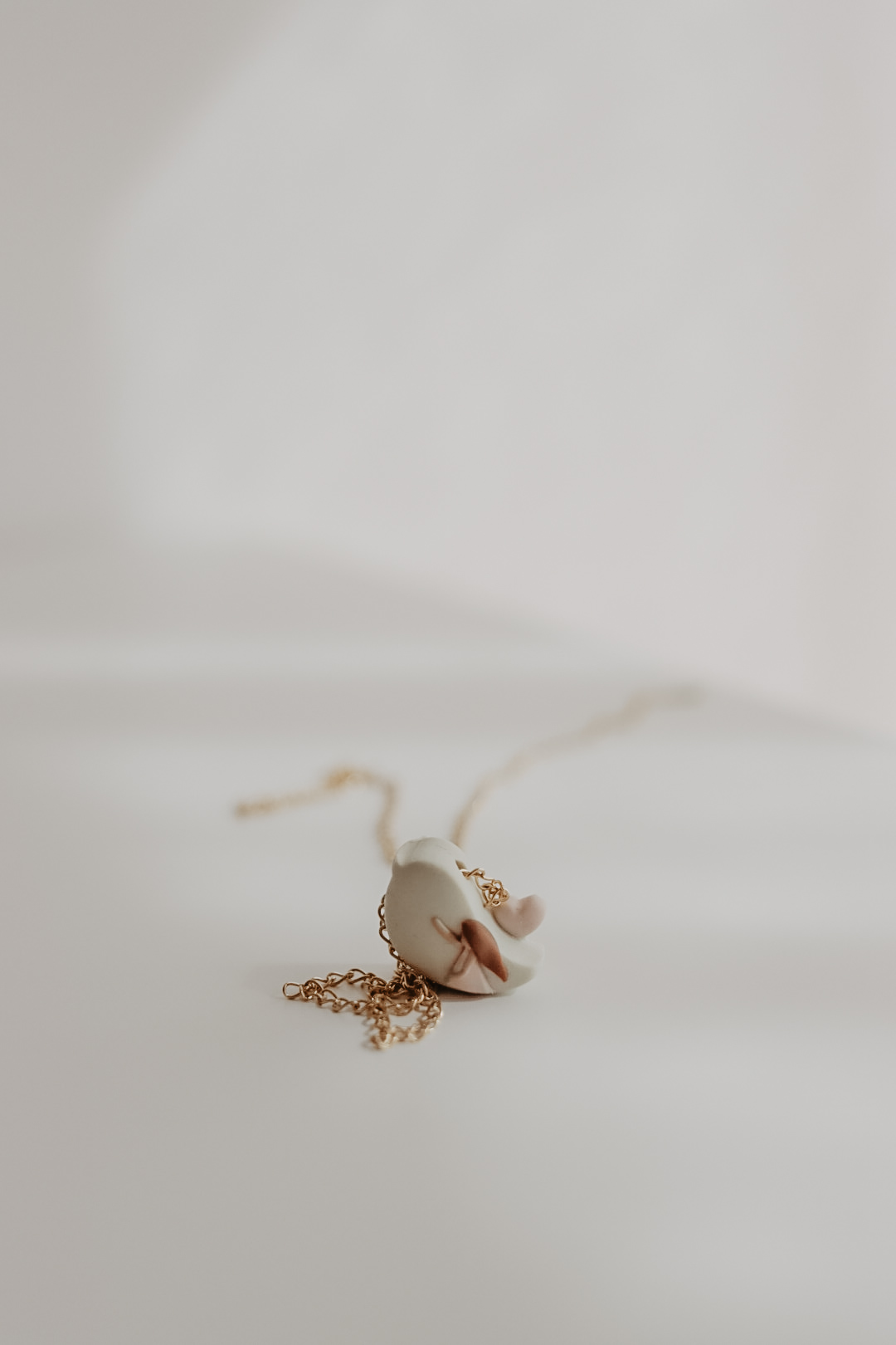 O Pássaro - Associação Portuguesa da Fertilidade Colar com pendente branco em forma de meia-lua e detalhes em rosa e castanho