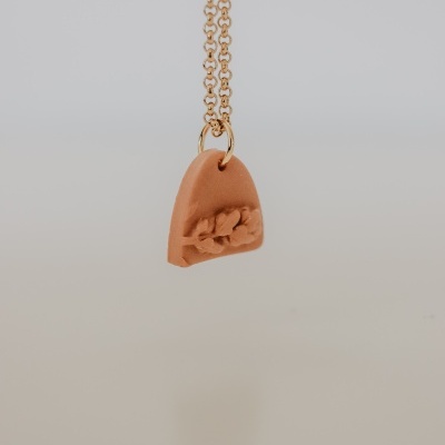 Colar com pendente terracota e corrente dourada em fundo cinzento claro
