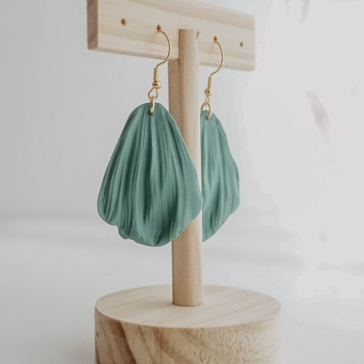 Brincos verdes com textura pendurados em suporte de madeira