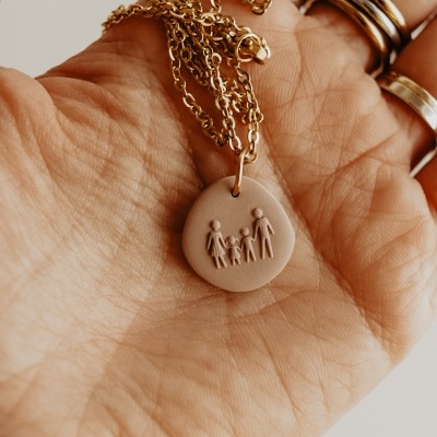 Colar com pendente redondo de figura de família cor de rosa claro e corrente dourada na mão.