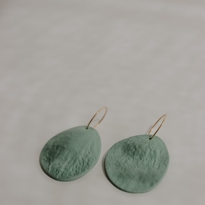 Brincos ovalados verdes com argolas douradas sobre fundo claro.