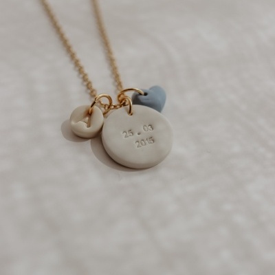 Colar dourado com três pendentes bege e azul num fundo claro texturado