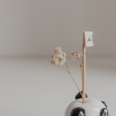 Vaso em cerâmica branco com padrão panda segurando flores secas e uma bandeira pequena branca