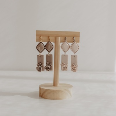 Brincos pendentes castanhos com flores em suporte de madeira.