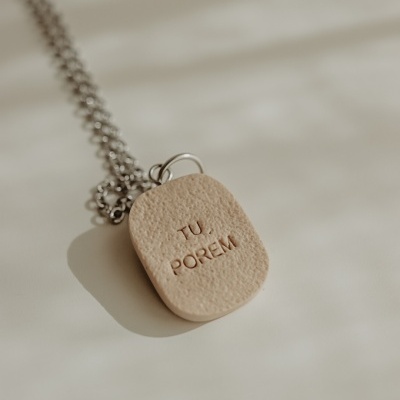 Colar com pendente retangular bege com texto TU, PORÉM gravado.