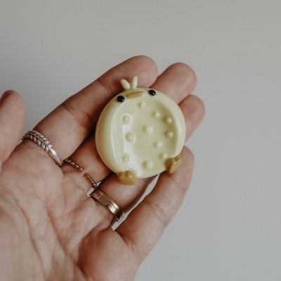 Pequena figura amarela com bolhas, vista numa mão com anéis