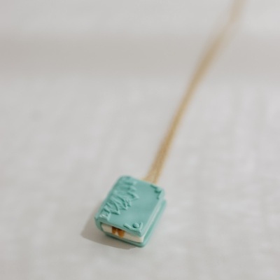 Colar com pendente mini livro azul turquesa com relevo e corrente dourada