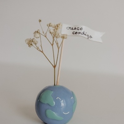 Vaso cerâmico azul com continente verde, flores secas brancas e bandeira com texto