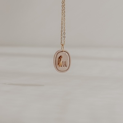 Colar dourado com pendente oval com letras I e M