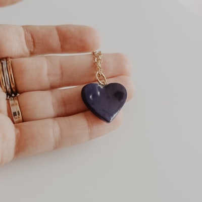 Colar com pendente de coração azul escuro em corrente dourada na mão
