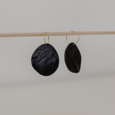 Brincos pendentes pretos com argolas douradas em suporte de madeira