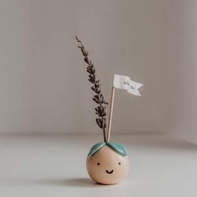 Objeto decorativo em cerâmica com rosto sorridente e ramo de lavanda