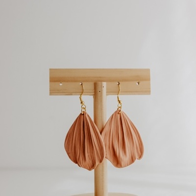 Brincos de tecido cor de rosa em forma de pétalas num suporte de madeira