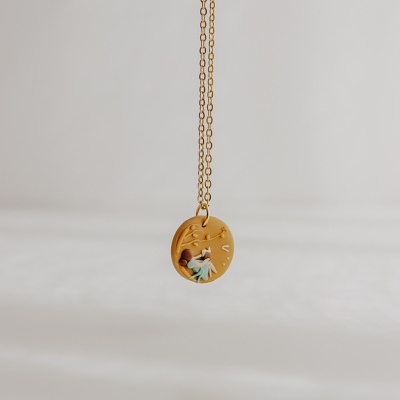 Colar dourado com pendente redondo com figura pequena detalhada em fundo cinza