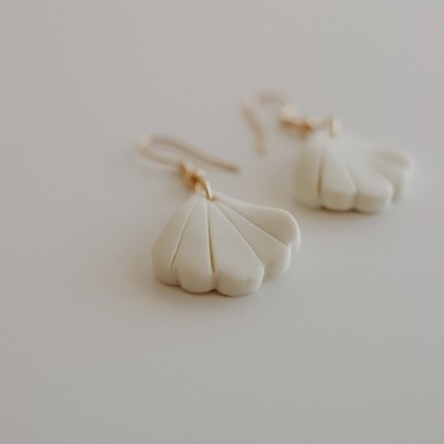 Brincos pendentes brancos com argolas douradas sobre superfície branca